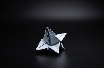 A single geometric origami sculpture in matte silver displayed on a black background, showcasing intricate folds and a minimalist, modern design illuminated by soft lighting