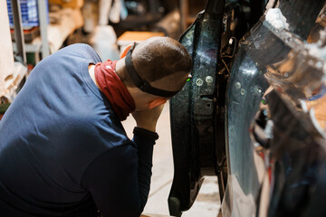 Car Mechanic Inspecting Vehicle Bodywork in Dimly Lit Garage