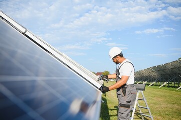 Naklejka premium Indian worker with screwdriver works on solar panels. Renewable energy