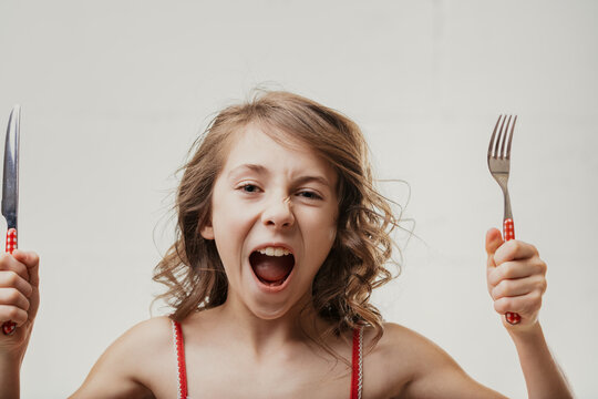 Hungry girl shouting and holding fork and knife