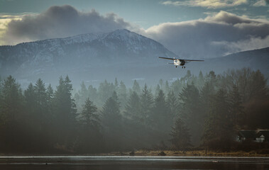 The early morning sun rises over the mountains in Comox, British Columbia as a Cessna 172 single engine aircraft comes in for a landing.