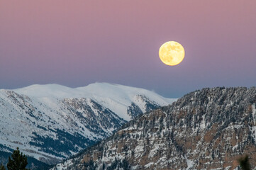 Salida de la luna llena en un paisaje de invierno. Montañas nevadas en los pirineos catalanes, con un atardecer rojizo.