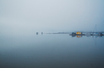 Yellow Boathouse stands out amongst the thick fog along the waterfront. Morning Fishing Scene.