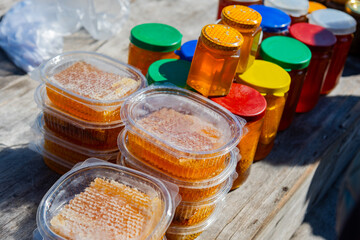 Plastic containers and glass jars of wholesome natural honey on a wooden table for sale to tourists and visitors.