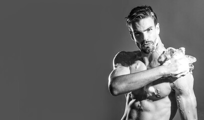 Body care, skincare and spa. Muscular man taking refreshing shower and washing body with soapy sponge. Handsome male taking shower with moisturizing gel. Black and white. Copy space for advertising.