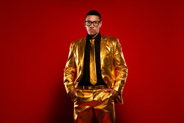 Charismatic young male posing in a golden suit against a vibrant red backdrop, exuding confidence...