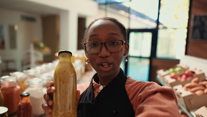 POV zero waste eco store owner filming social media ad to present their new homemade sauces and natural bio products. Woman promoting sustainable lifestyle and eco food online. Handheld shot.