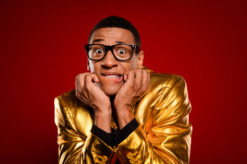 Young man in golden jacket posing playfully against a vibrant red backdrop, embodying a mix of elegance, humor, and charm