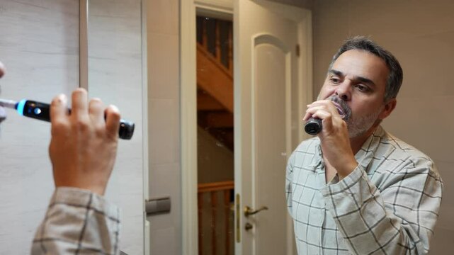Mature man brushing his teeth with an electric toothbrush in front of a mirror, slow motion footage