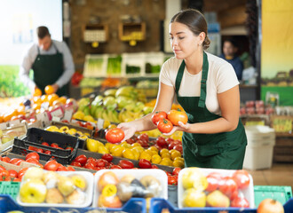 Young female seller wearing apron holding fresh ripe tomatoes on market