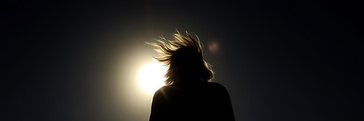Fototapeta premium Silhouette of a person in sunlight with wind creating dynamic motion in hair
