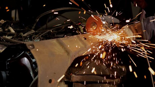 A man cuts metal in a car. The car is rusting in a junkyard. Scrap metal that is disposed of. A man holds a grinder, saws iron with a disk