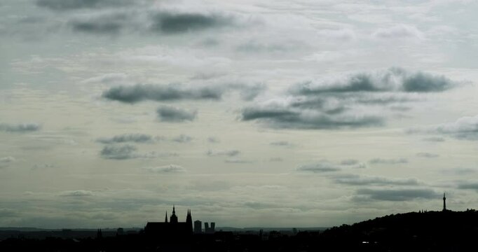 Prague Castle and Petř&iacute;n Tower Silhouetted on the Horizon Beneath a Pale Gray High Cloud Canopy with Fast Moving Low Clouds Playing Light and Shadow Across the Sky in 4K Time Lapse