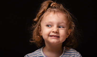 Fun adrabale baby girl looking with skeprical facial curious sly emotion face looking looks away up with curly hair on black studio background with empty copy space. Closeup