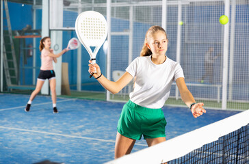 Teenage girl playing padel game on tennis court
