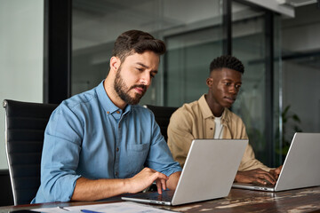 Two busy diverse male employees using laptop computer talking in office. Professional young...