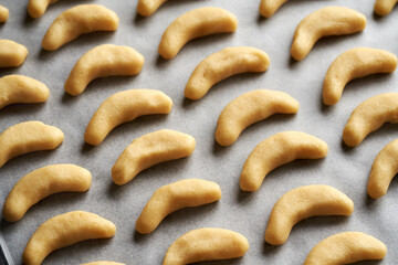 Raw sweet pastry dough rolls on a baking sheet - preparation of homemade vanilla crescents or Kipferl, German Christmas cookies
