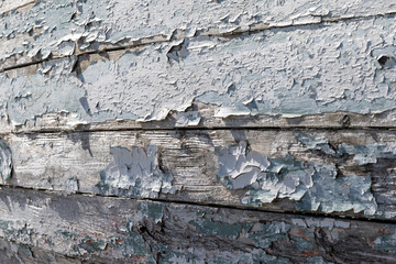 A horizontal wooden exterior wall, white color, of textured rough clapboard siding.  The wood is grainy and there are overlapping boards. The wall has bumps and uneven surfaces with peeling paint.
