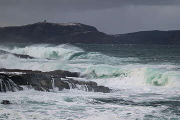 An angry turquoise green color massive rip curl of a wave as it rolls along a beach. The white mist and froth from the wave are foamy and fluffy. The Atlantic Ocean in the background is deep blue. 