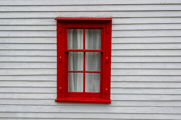 The exterior of a white wooden exterior shed wall with a red frame and closed glass single hung window. Looking through the window you can see green braided fishing rope stacked inside the building.