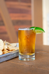 A small clear sampler glass filled with a cold IPA beer. The cold golden Mexican beer sits on a bar at a craft brewery with a slice of lime on the rim of the glass as a garnish. Its an alcoholic ale.