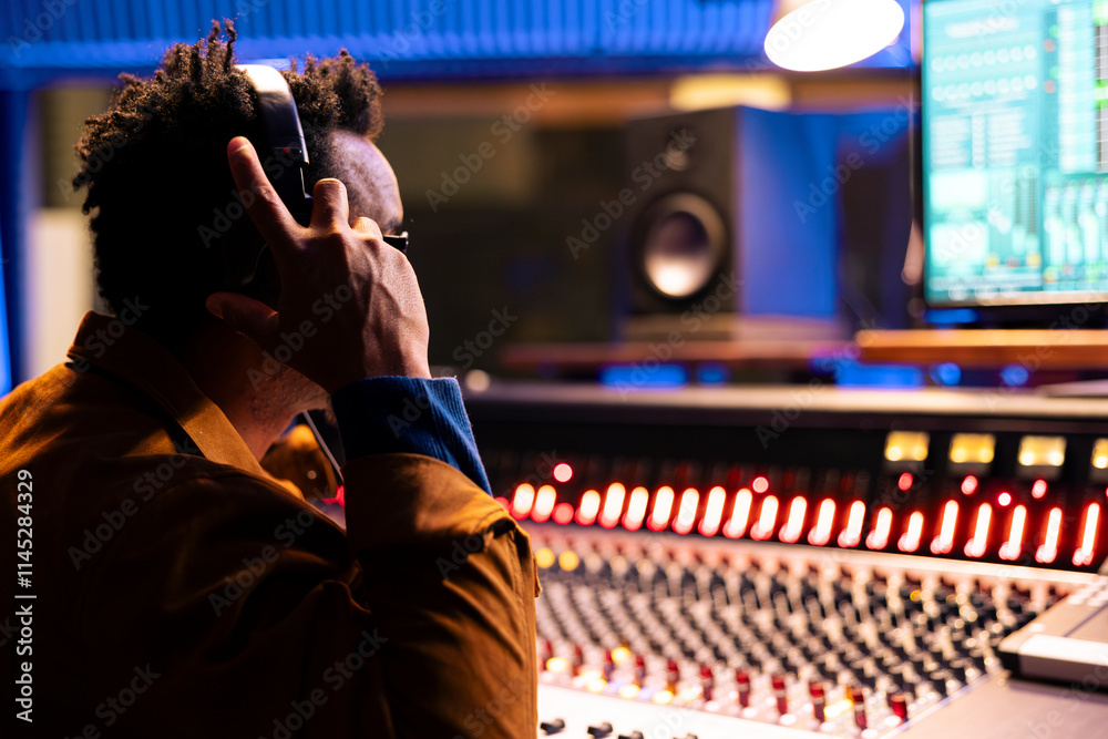 Poster Music producer using headphones when editing and processing tracks, recording in control room at professional studio. Audio engineer pressing buttons to add sound effects in post production.