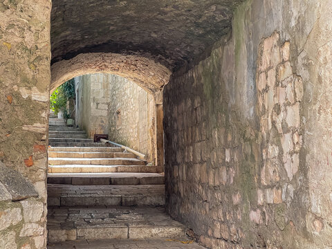 Korcula, Croatia - June 30, 2024: Look into alley with mostly steps and part under buildings. Green foliage in backj and front