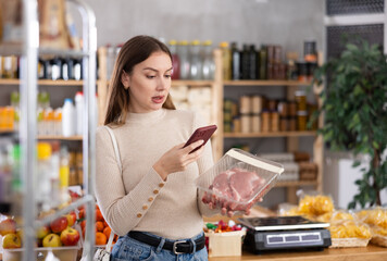 Young female shopper scanning qr code for packaged raw pork meat in grocery store