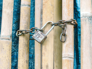 A rusty padlock and chain on a bamboo fence.
