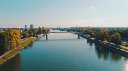 Obraz premium Aerial view of a bridge over a calm river, lined with trees and buildings in the background.