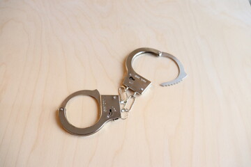  A pair of handcuffs on a wood background. A toy representing metal handcuffs. Criminal capture and...