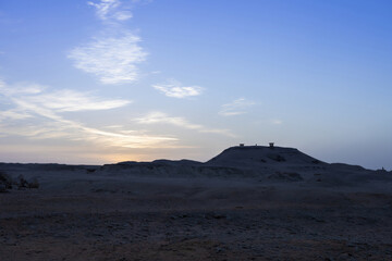 Desert landscape with expansive sky at dusk and silhouettes of structures