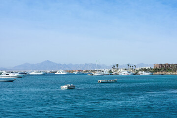 Serene coastal view with boats and distant mountains under clear blue sky