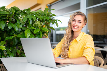 Worldwide work: Happy female developer working on laptop at outdoor restaurant. Smiling confident...
