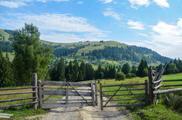 Fototapeta premium Scenic view of a rustic wooden gate opening to a lush green valley surrounded by mountains under a clear sky. Perfect for conveying natural beauty and tranquility. Carpathian Mountains, Ukraine 