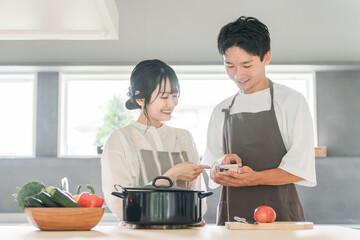 スマホを見ながらキッチンで料理を作る夫婦（レシピサイト・レシピアプリ）
