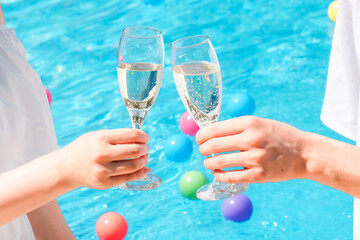 バカンス・リゾートホテルのプールサイドでシャンパングラスで乾杯するカップルの手元  © buritora