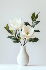 Obraz premium Two creamy white magnolia blossoms in a simple white vase against a light gray background.