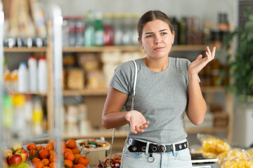 Puzzled woman forgot what she wanted to buy from the groceries in the supermarket. Customer remembers a list of purchases and food