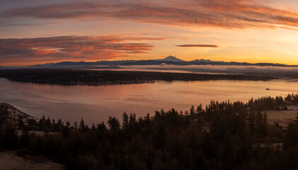 Aerial view of a dramatic sunrise over Lummi island and Hale Passage with Mt. Baker in the background. A ferryboat can be seen crossing the pass across to Gooseberry Point on the mainland.