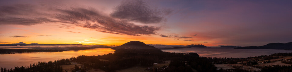 Aerial view of a dramatic sunrise over Lummi island and Hale Passage with Mt. Baker in the background. A ferryboat can be seen crossing the pass across to Gooseberry Point on the mainland.