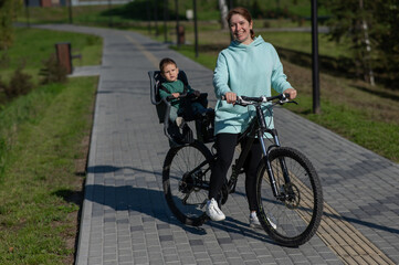 Caucasian woman riding a bicycle with her toddler son sitting behind her in a child seat. 