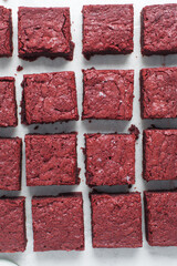 Overhead view of sliced red velvet brownies on a white background, Top view of sliced fudgy red velvet brownies on a white marble tray