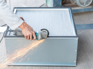 Worker use a grinder to cut the edges of the air filter metal box.