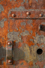 Detail shot of hinges on a rusty red painted metal door. Textural study with peeling, distressed rusted red metal paint on an old door.