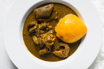Overhead view of Nigerian banga soup and starch with fish and beef in a white plate, top view of palm nut soup in a large dinner plate, traditional palm nut soup in a white dish