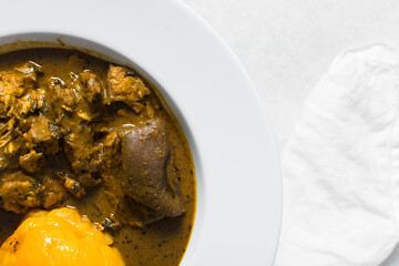 Overhead view of Nigerian banga soup and starch with fish and beef in a white plate, top view of palm nut soup in a large dinner plate, traditional palm nut soup in a white dish