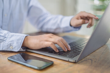 Close up of businessman working with laptop computer on table at office. Business man hands typing on laptop, online working, surfing the internet at workplace