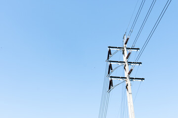 Cement pole with cross beams supports power lines against a clear blue sky.
