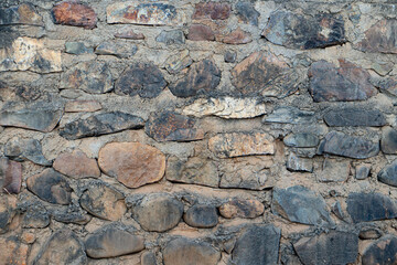 Rough stone wall made of various sized and colored rocks. Creating a textured and uneven surface.